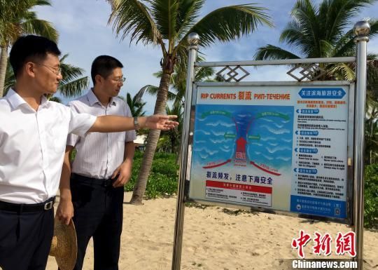  中国首批裂流警示标识已经在海南三亚、陵水的重点滨海旅游区树立。8月31日，海南陵水黎族自治县县委常委、副县长孟庆垒（左）向记者介绍树立在陵水重点滨海旅游区的裂流警示标识。　阮煜琳　摄