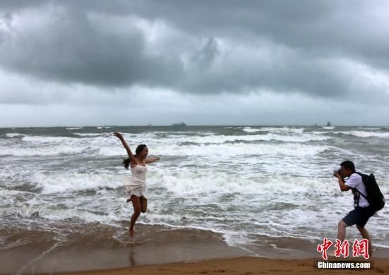 资料图：游客在乌云密布、大浪翻滚的三亚湾游玩嬉戏，享受风雨带来的清凉。中新社发 尹海明 摄