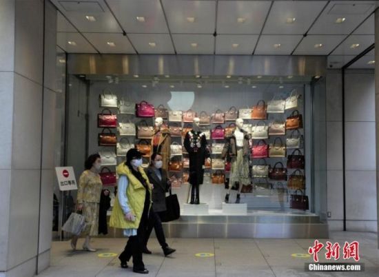 资料图：东京民众戴口罩经过商场橱窗。 中新社记者 吕少威 摄