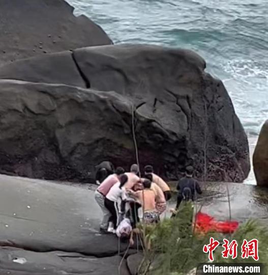图为游客在海南文昌石头公园脱衣拧成长绳抛下礁石救人现场视频截图。　符宇群　摄