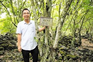 钟邦富在自家黄皮果园里和百年黄皮树合影。 （秀英区永兴电商扶贫中心供图）